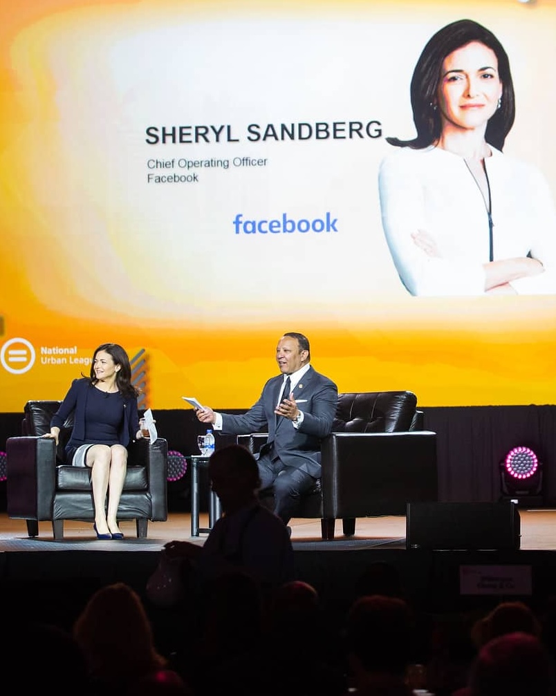 Sheryl Sandberg speaking on stage at a Facebook event